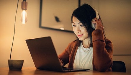 Girl smiling, looking at laptop screen, wearing headphone