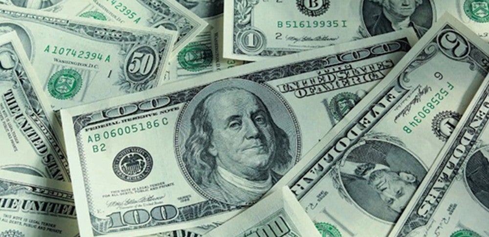 A collection of United States paper currency is spread out in a random arrangement. The bills feature various denominations, with visible numbers such as '50', '100', and '1'. The setting is a close-up view, emphasizing the green and white color palette and intricate details of the currency. Some areas of the bills are blurred, obscuring certain features.