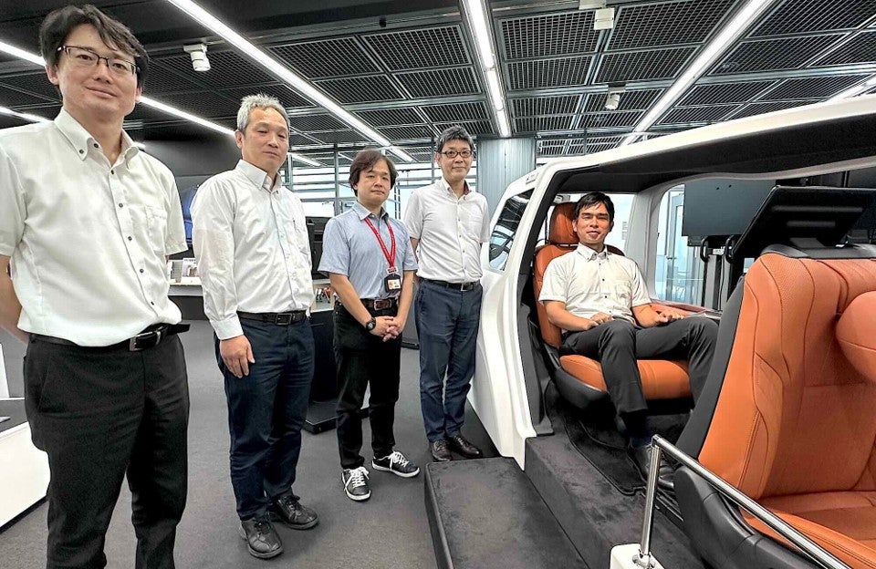 展⽰エリアのデモ⽤シートに座るディアイスクエア飯⽥⽒と制御システム開発室の皆様