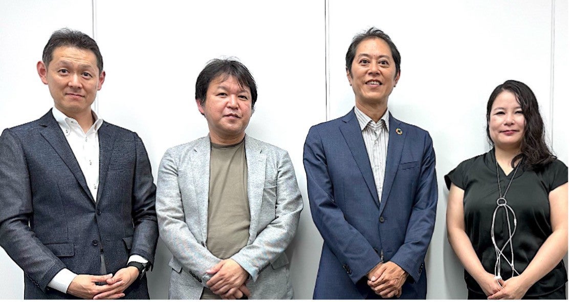 4人が白い壁の前に立って、写真のポーズをとっています。
